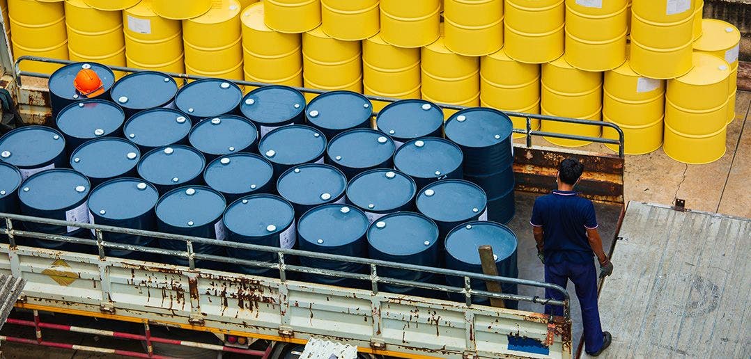 Blue steel drums packed in the back of a moving truck in a warehouse with yellow steel drums stored behind them in the warehouse.
