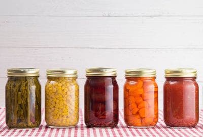 multiple glass jars of vegetables pickles and jams.