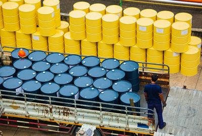 Blue steel drums packed in the back of a moving truck in a warehouse with yellow steel drums stored behind them in the warehouse.