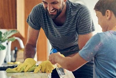 A father and child use a spray bottle and rag to clean the kitchen