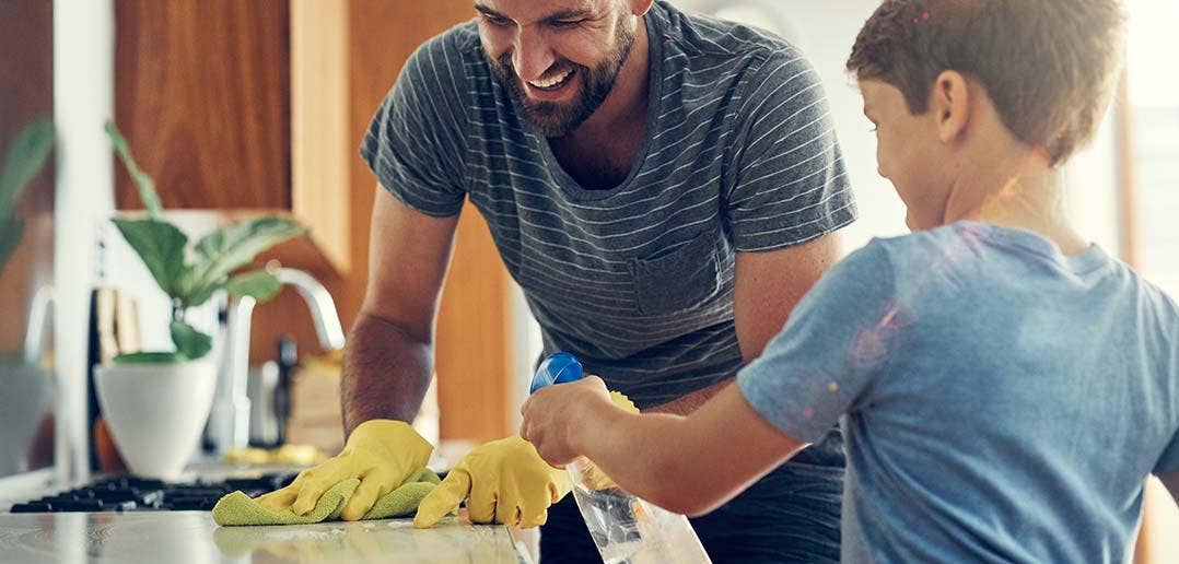 A man and child use a spray bottle and rag to clean the kitchen.