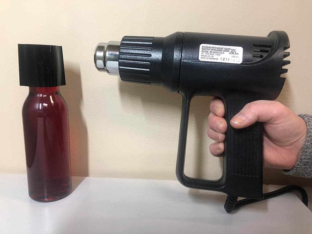 Bottle with heat gun pointed at shrink band