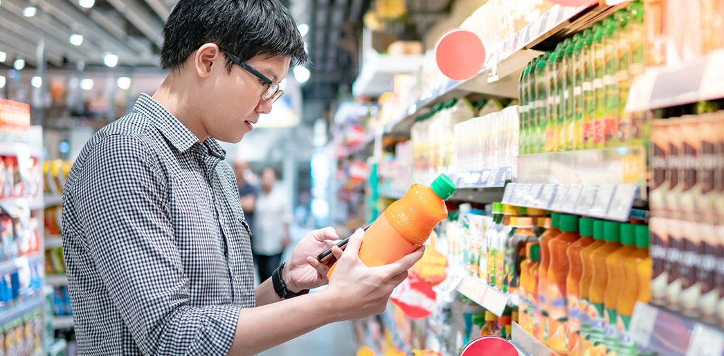 An image of a man looking at a beverage bottle in a grocery store